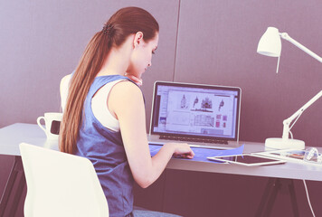 Young woman sitting at the desk with instruments, plan and laptop.