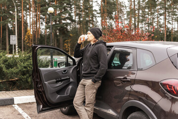 male driver drinking coffee standing beside the car. rest on a long journey. coffee stop.