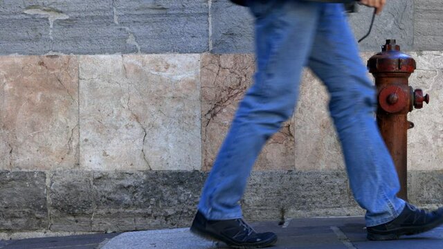 person wearing jeans and black shoes walks in front of the wall and an old red fire hydrant