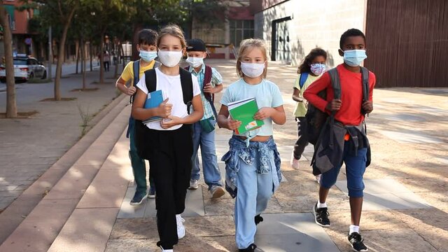 Portrait of tween boys and girls in protective masks with backpacks going to school lessons on sunny autumn day. New lifestyle during coronavirus pandemic