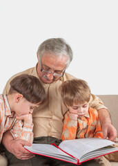 Positive elderly man reading a book for his grandchildren sitting on sofa.