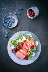 Modern style gourmet duck breast filet with rocket salad and cranberry relish offered as close-up on a design plate with copy space