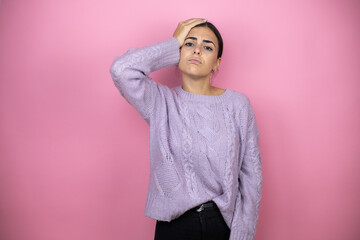 Beautiful woman wearing a casual violet sweater over pink background putting one hand on her head...