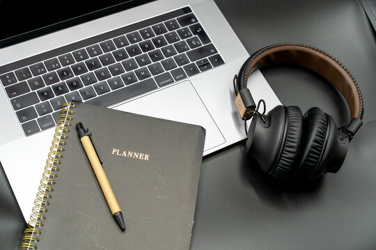 Concepto de teletrabajo desde casa. Libreta y auriculares sobre port&aacute;til en fondo negro.