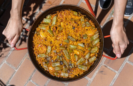 Mujer sujeta paella valenciana con las manos.