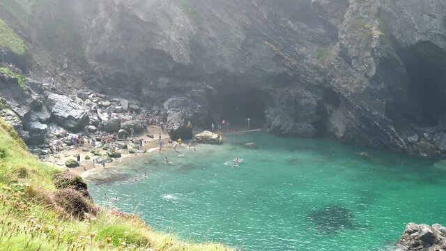 People swimming in turquoise water of Tintagel Cove, United Kingdom surrounded by high cliffs.