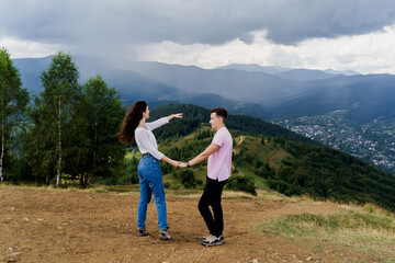 Fototapeta na wymiar Girl points her boyfriend at rain far away. Couple looking at the mountain hills before raining. Feeling freedom together in Karpathian mountains. Tourism travelling in Ukraine