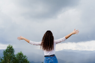 Fototapeta na wymiar Feeling freedom in Karpathian mountains. Tourism travelling in Ukraine. Girl girl raised her hands up and enjoys the mountain hills view.