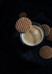 Creamy coffee cup surrounded by chocolate cookies and another one on top of the cup.