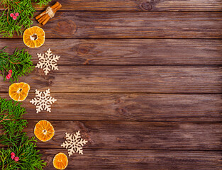 Christmas or New Year wooden background with Christmas tree decorations, red berries, cinnamon, orange slices and juniper branches.