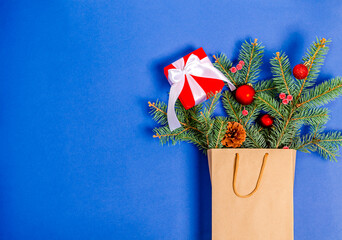 Christmas toys, pine cone, gift box, fir branch in a shopping bag on a blue background.