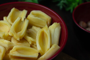 Buah Nangka or Jackfruit, one of tropical fruits popular in Indonesia. Cut into  half on red bowl and the seeds at behind. Dark wooden background. 