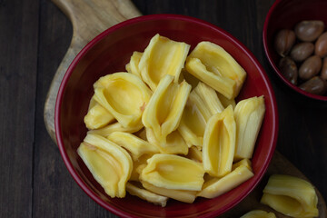 Buah Nangka or Jackfruit, one of tropical fruits popular in Indonesia. Cut into  half on red bowl and the seeds at behind. Dark wooden background. 
