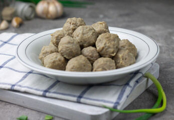 Bakso Sapi or Meatball traditional popular street food in Indonesia, served with clear soup, and noodles. Grey wooden background. Selective focus, copy space. 
