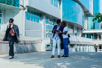 Two male colleagues reviewing their documents outside while their female colleague is talking on the phone.