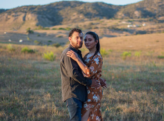 A romantic and lovely latin couple hugging each other in a beautiful sunny day with a dry grass field and a sunset in the background