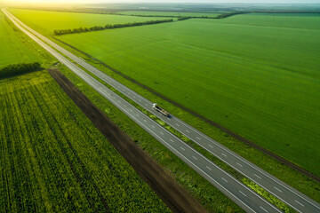 blue truck driving on asphalt road along the green fields. seen from the air. Aerial view landscape. drone photography.  cargo delivery. Sunset time