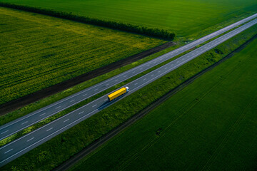 yellow truck with container on highway,  driving on asphalt road along the green fields. seen from the air. Aerial view landscape. drone photography.  cargo delivery cargo transportation