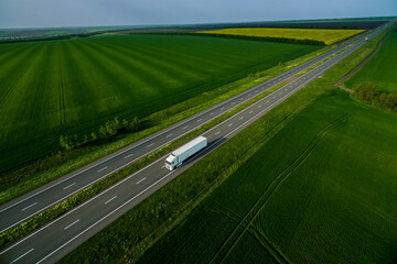 white truck driving on asphalt road along the green fields. seen from the air. Aerial view landscape. drone photography.  cargo delivery Left side traffic
