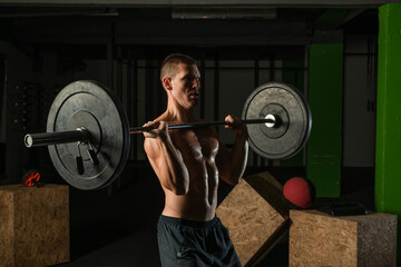 Fototapeta na wymiar Muscular man working out with a barbell at his homemade gym