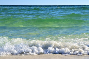 Waves from the ocean seethe and foam on the shore, forming white lambs and foam, close up