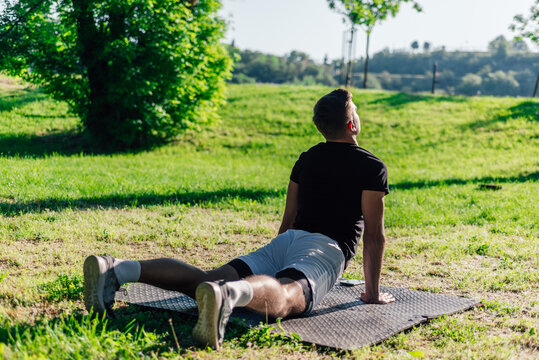 Young caucasian man practicing yoga on a mat outdoors at the park in cobra pose