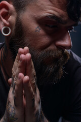 Close up portrait of a bearded man with tattoos on his hands, face and neck wearing black shirt.