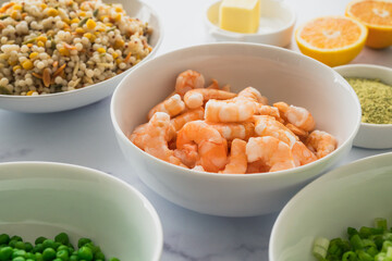 Blend of couscous, orzo, garbanzo beans, and red quinoa, shrimps, green peas, and chopped green onion in bowls close up on marble background