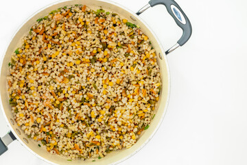 A savory blend of pearled couscous, orzo, baby garbanzo beans, and red quinoa close up on frying pan on white background, flat lay with copy space
