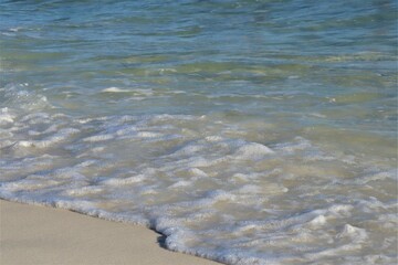 A wave rolls back from the shore, exposing light, clean sand and foaming at its edge, viewed from above
