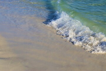 Waves from the ocean seethe and foam on the shore, forming white lambs and foam, close up