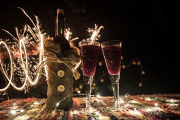 Red wine in crystal glass with bottle on colorful carpet with creative New Year artwork decorations. Copy space