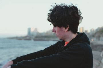 Fototapeta premium young man sitting on the rocks looking at the sea, copy space, tourism, reflection, social media, man