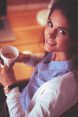 Portrait of relaxed young woman sitting at her desk holding cup of coffee