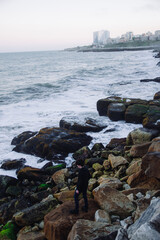 young man standing on the rocks by the sea while the waves crash, travel plan, tourism campaign, summer, sea, beach, cool