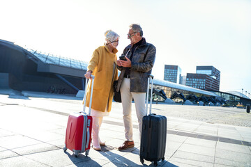 Seniors couple in masks using mobile phone on the train station.