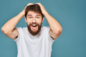 A bearded man in a white T-shirt gestures with his hands emotions blue background