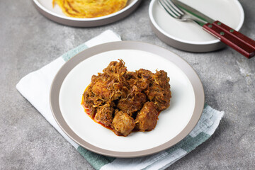 Ayam Kari or chicken curry, Indonesian traditional food served on ceramic plate, very popular at hari raya celebration food with roti canai, lontong, buras and ketupat. Grey wooden background.