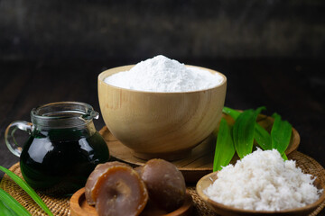 Preparation ingredients to make Klepon Rice Ball cake, Indonesian traditional sweet boiled cake, made from glutinous rice flour, pandan leaves, grated coconut, and palm sugar. Dark wooden background  