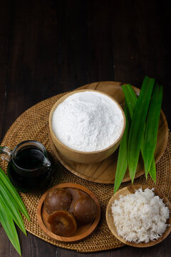 Preparation ingredients to make Klepon Rice Ball cake, Indonesian traditional sweet boiled cake, made from glutinous rice flour, pandan leaves, grated coconut, and palm sugar. Dark wooden background  