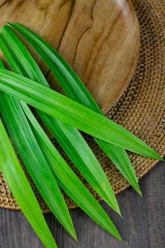 Close up view of pandan leaves or pandanus leaves on wooden brown plate. Pandan leaves usually use as food coloring with aromatic smell. Dark wooden background. 