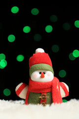 Muñeco de nieve hecho de tela con bufanda y gorro y luces de navidad de fondo 