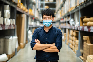 Fototapeta na wymiar male manager wearing medical mask with arms crossed in warehouse store during coronavirus (covid-19) pandemic.