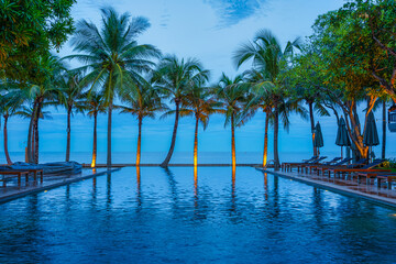 Fototapeta premium swimming pool with background of coconut tree and sea at beachfront resort