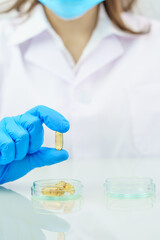 Scientist hands putting in nitrile blue latex gloves  holding Omega 3 capsule in labcoat