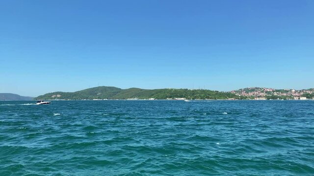Footage of a dry cargo vessel and boats passing on Bosphorus strait in Tarabya area of Istanbul. Kanlica / Beykoz area of Asian side is in the view. It is a sunny summer day. Camera pans right.