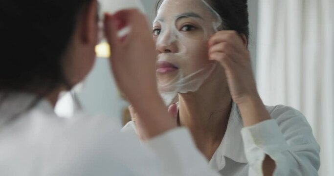 female Skin care concept young asian woman looking at mirror in the morning putting face mask young people using face pack at home