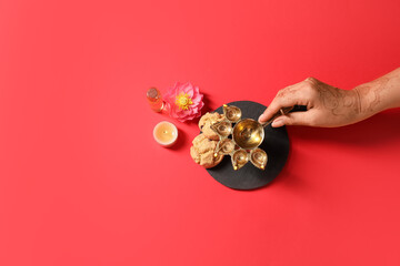 Female hand with diya lamp, burning candle, oil and cookies for celebration of Divaly on color background