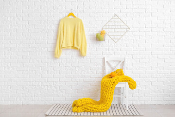 Chair with yellow plaid and knitting yarn near white brick wall