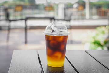 espresso shot mixed with orange juice on ice in plastic transparent glass with blurred coffee shop  background